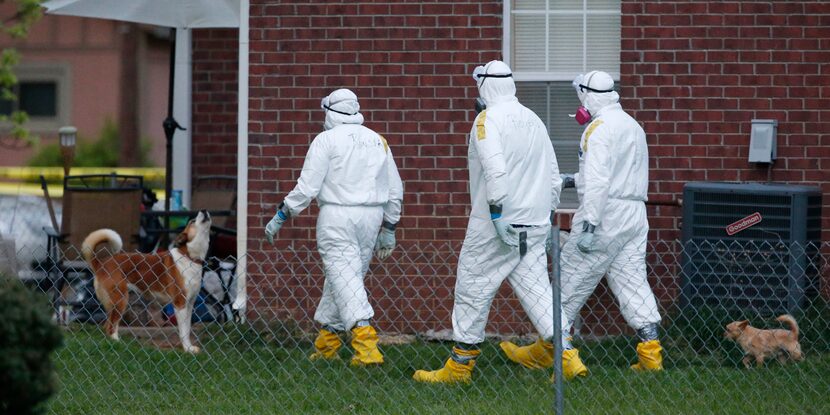 A dog barks at federal agents wearing hazmat suits as they inspect the grounds around the...