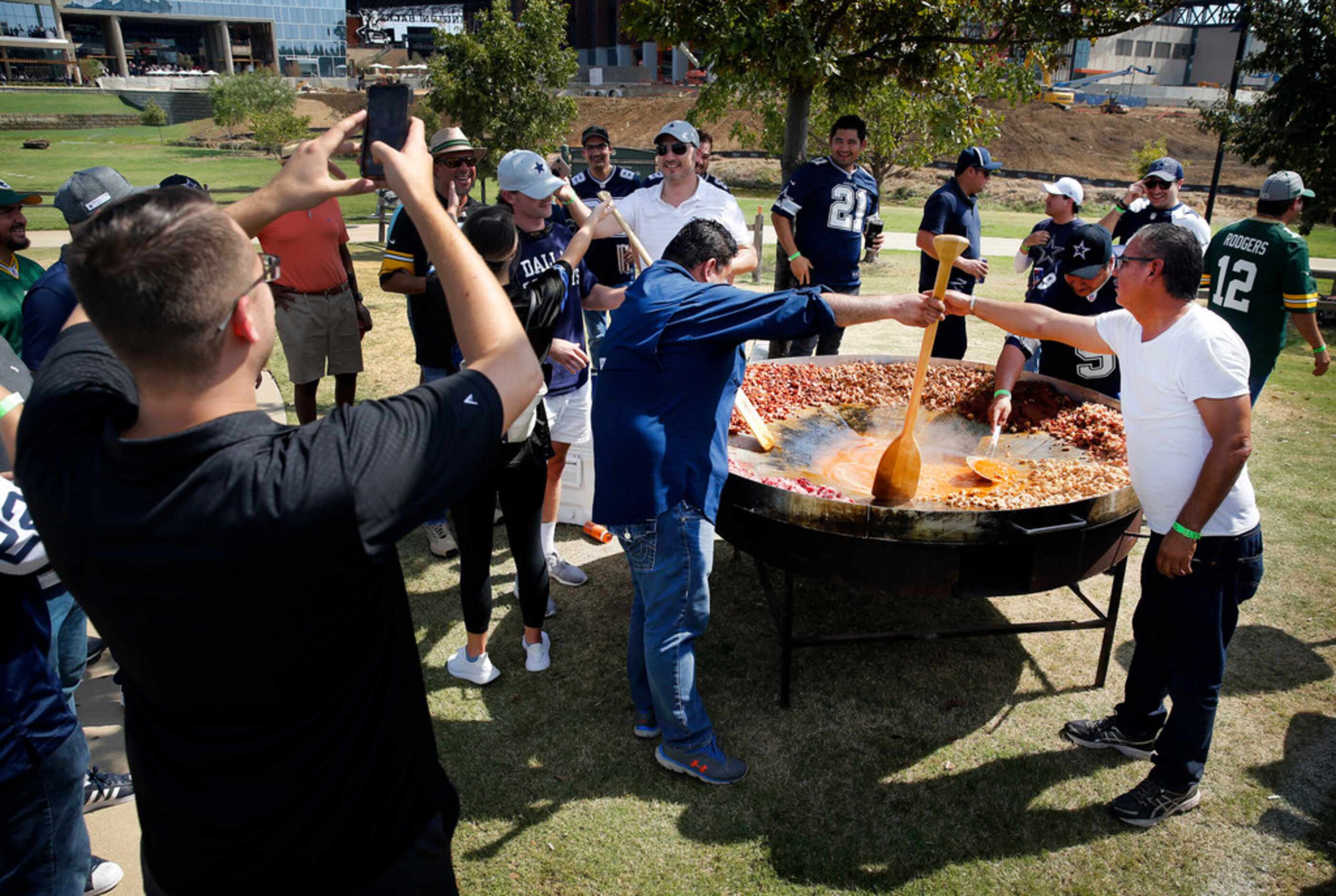 Dallas Cowboys fans use a canoe oar to stir discada, a mixed Mexican meat dish during a...
