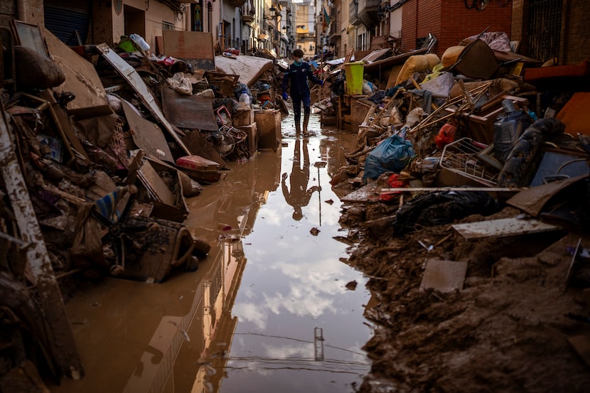 Una persona camina por la calle entre muebles y basura amontonada a los lados afectada por...