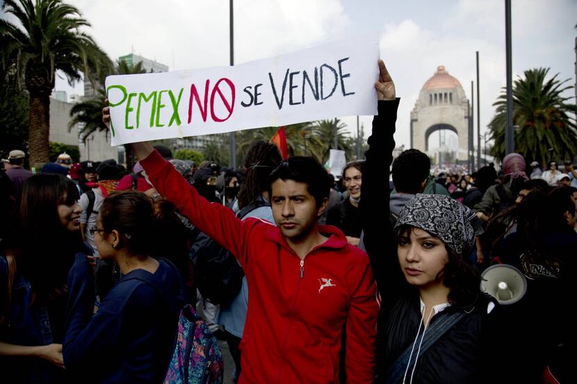 A couple holds up a banner about Mexico's state-owned oil company that says, "PEMEX is not...