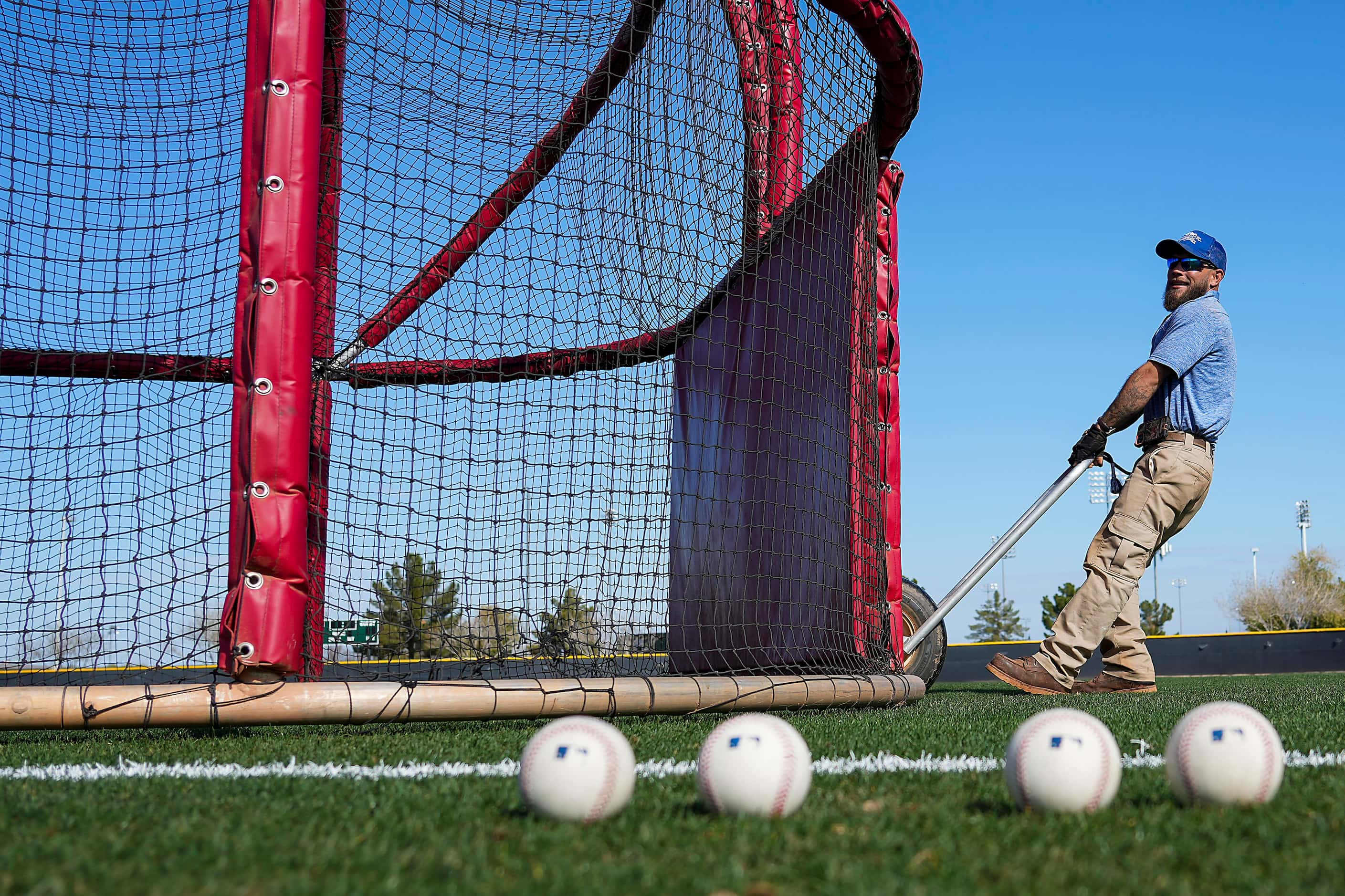 A groundskeeper moves a batting cage during a Texas Rangers spring training workout at the...