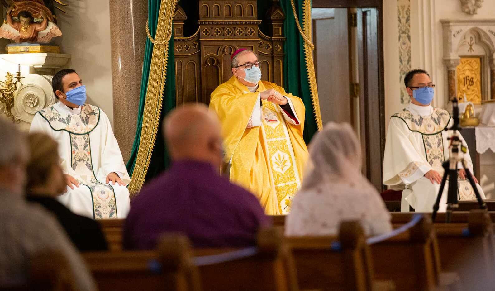 Bishop Michael Olson (center) rubs sanitizer on his hands during mass.
