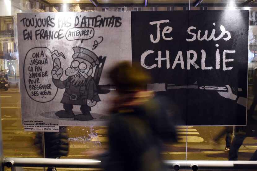 
A woman walks by a poster bearing the last cartoon of the late cartoonist Charb, affixed to...
