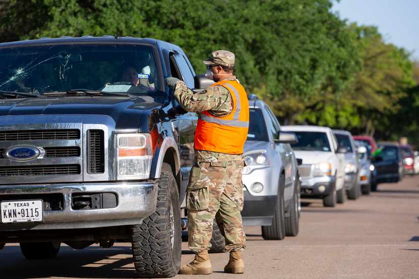 A member of the Texas National Guard picks up driver's information to receive food from the...