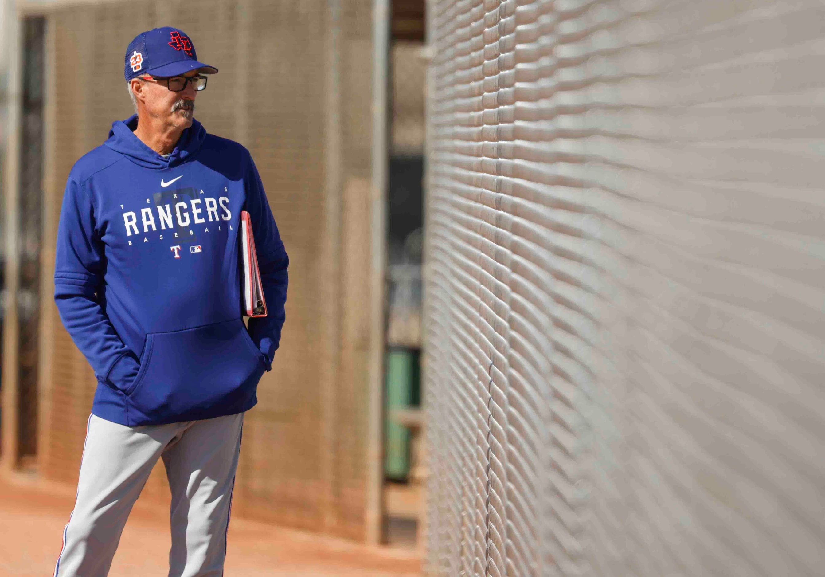 Texas Rangers pitching coach Mike Maddux looks out of the fence during a spring training...