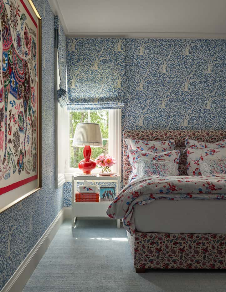Blue wallpaper in a bedroom matches the window coverings and an upholstered bed is covered...