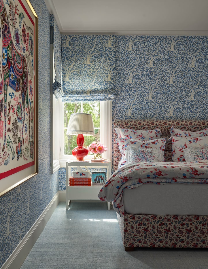 Blue wallpaper in a bedroom matches the window coverings and an upholstered bed is covered...