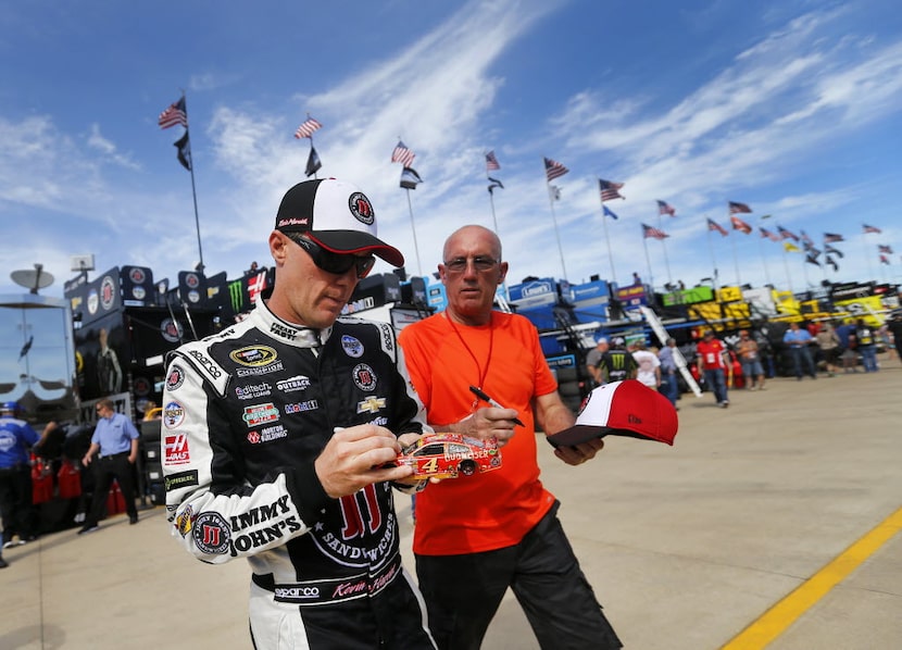 NASCAR Sprint Cup Series driver Kevin Harvick (left) signs autographs for a fan as he walks...