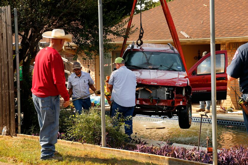 A wrecker crew uses a crane to lift a Jeep Grand Cherokee from a backyard pool on Clemson...