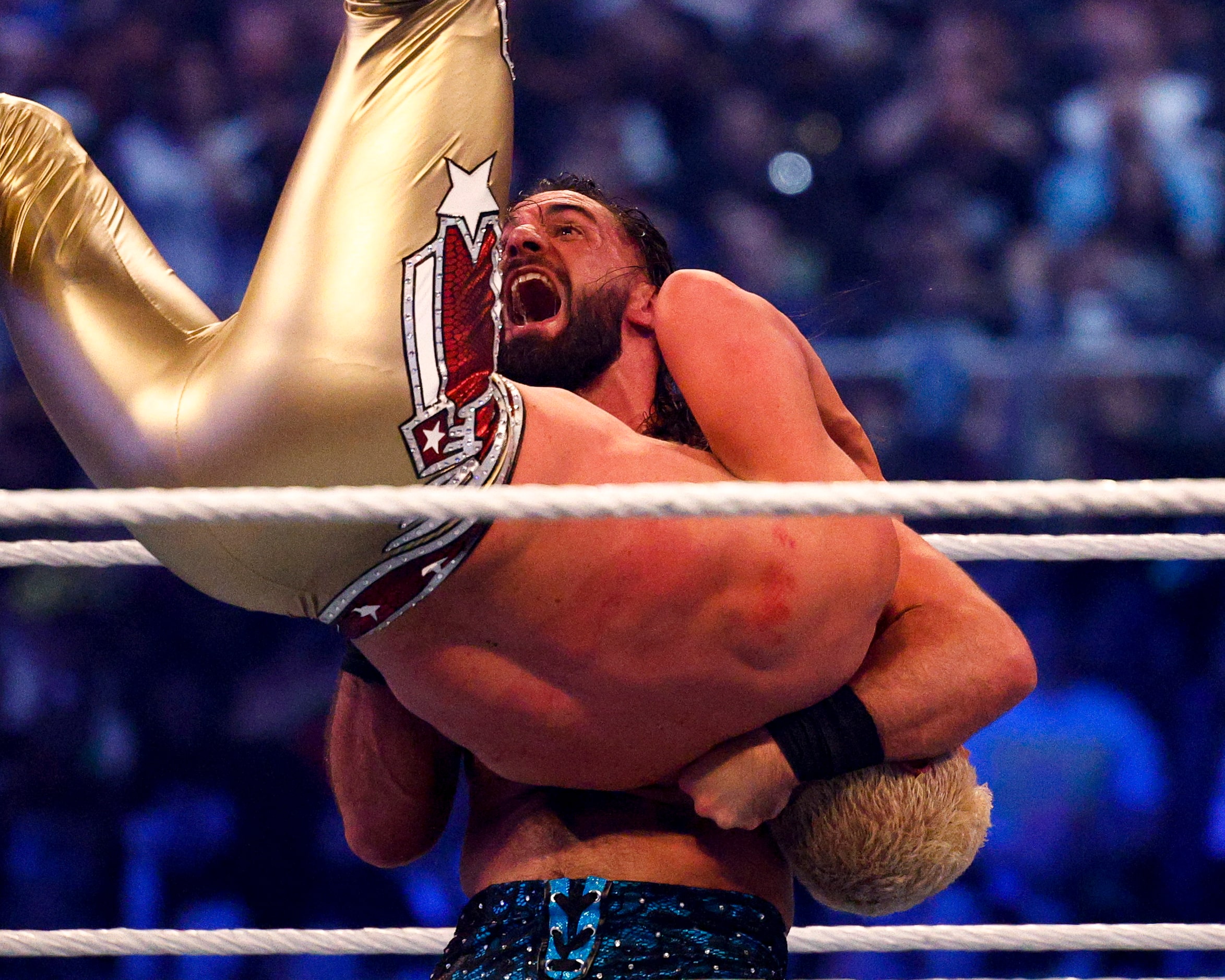 Seth Rollins (center) flips Cody Rhodes during a match at WrestleMania 38 at AT&T Stadium in...