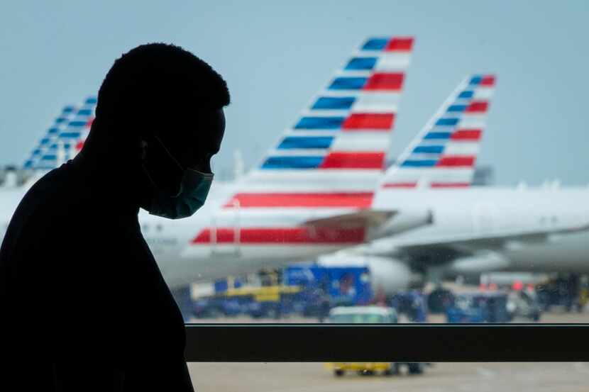 A man wearing face covering waits at a gate at Terminal E as American Airlines planes are...