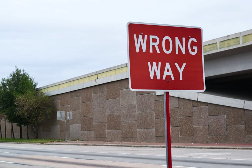 A Wrong Way sign on the side of a freeway frontage road in the city suburbs with an overpass...