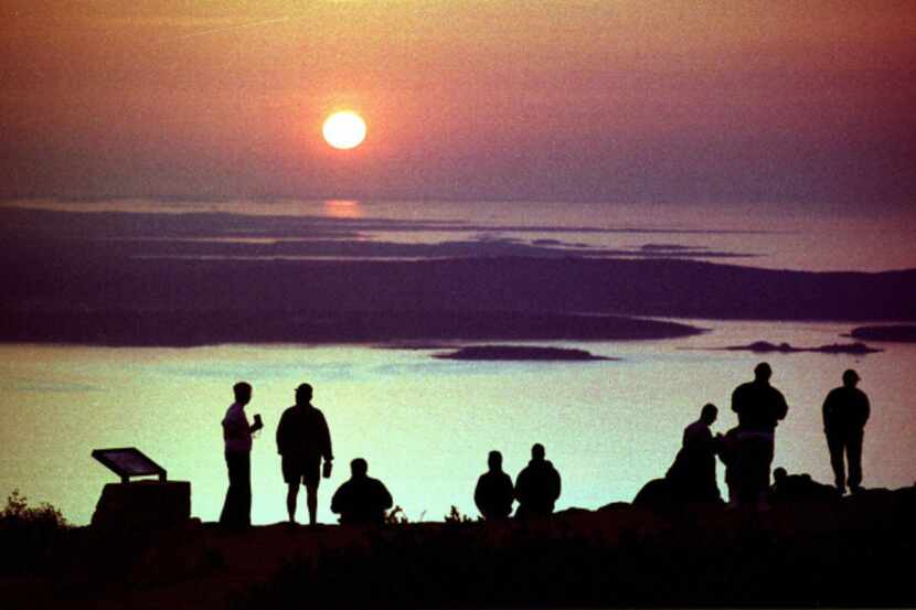 Visitors to Acadia National Park watch the sun rise from the summit of Cadillac Mountain, in...