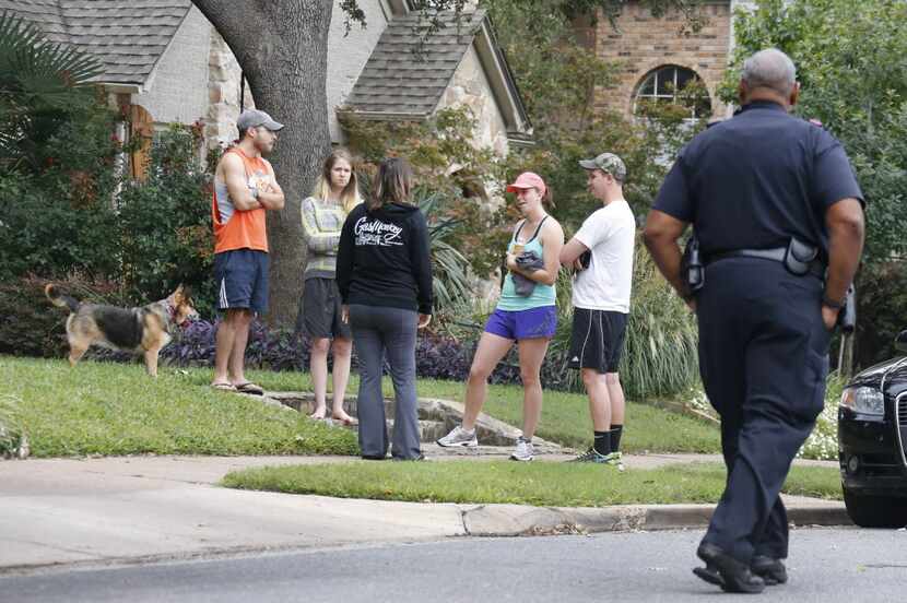 Residents along the street gather to discuss the day's events as officials guard the...