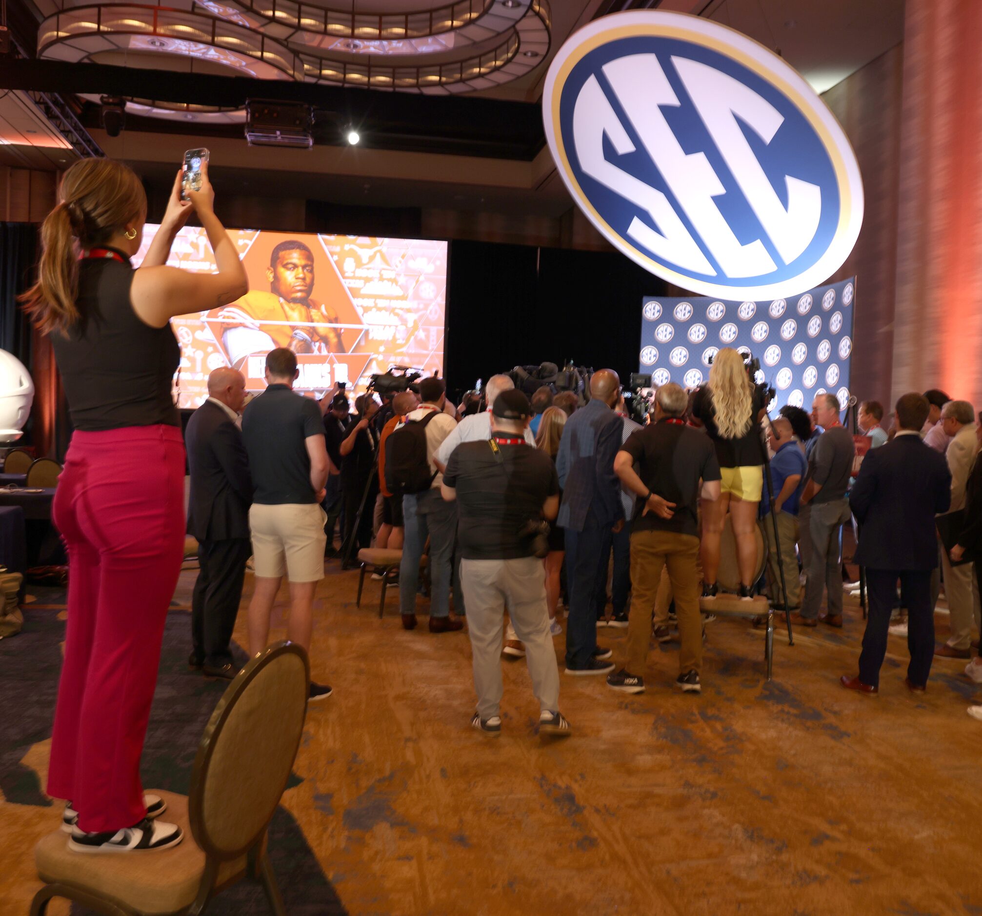 A media member utilizes a chair to be able to see Quinn Ewers over the crown gathered to ask...