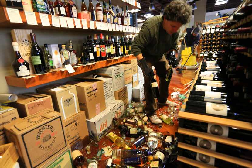 Dan Dawson cleans up his ruined inventory at his store, Back Room Wines, in Napa, Calif.,...
