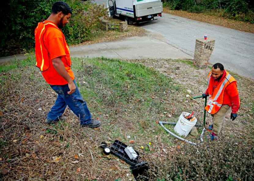 
Samuel Corley (left) and Cornelius Alfred  install a digital water meter at a home in Cedar...