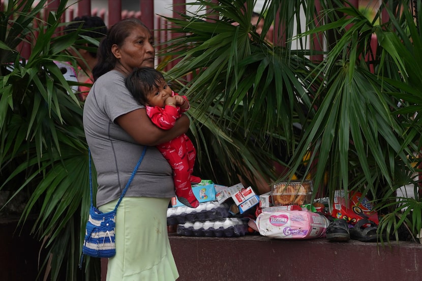 Una mujer sostiene a un bebé en brazos junto a varios objetos saqueados luego del paso del...