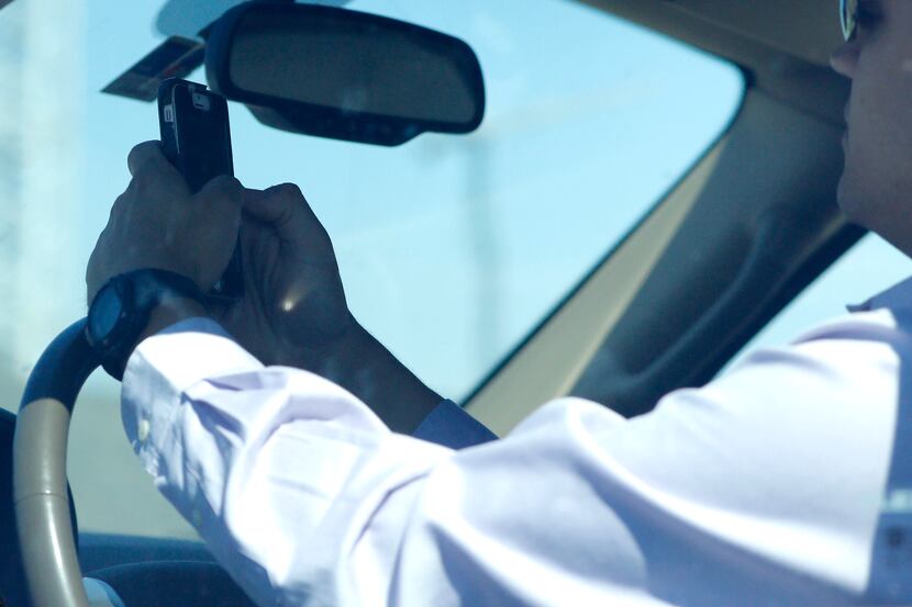 A man looks at his phone while driving down Woodall Rodgers Freeway in Dallas on July 16,...