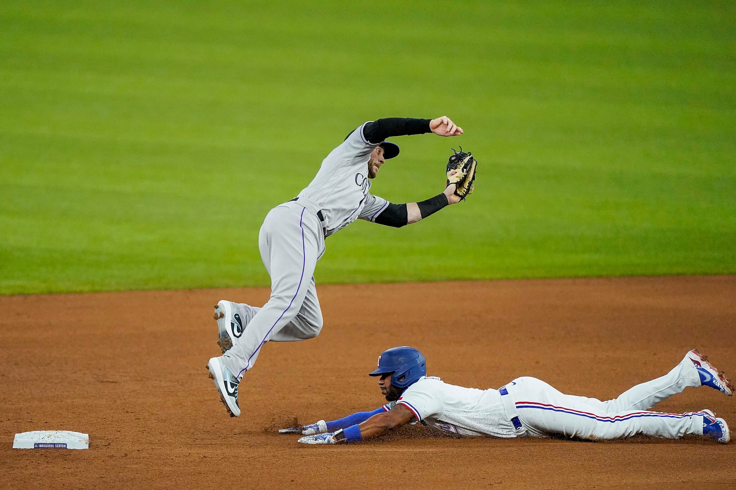 Colorado Rockies shortstop Trevor Story leaps over Texas Rangers shortstop Elvis Andrus to...