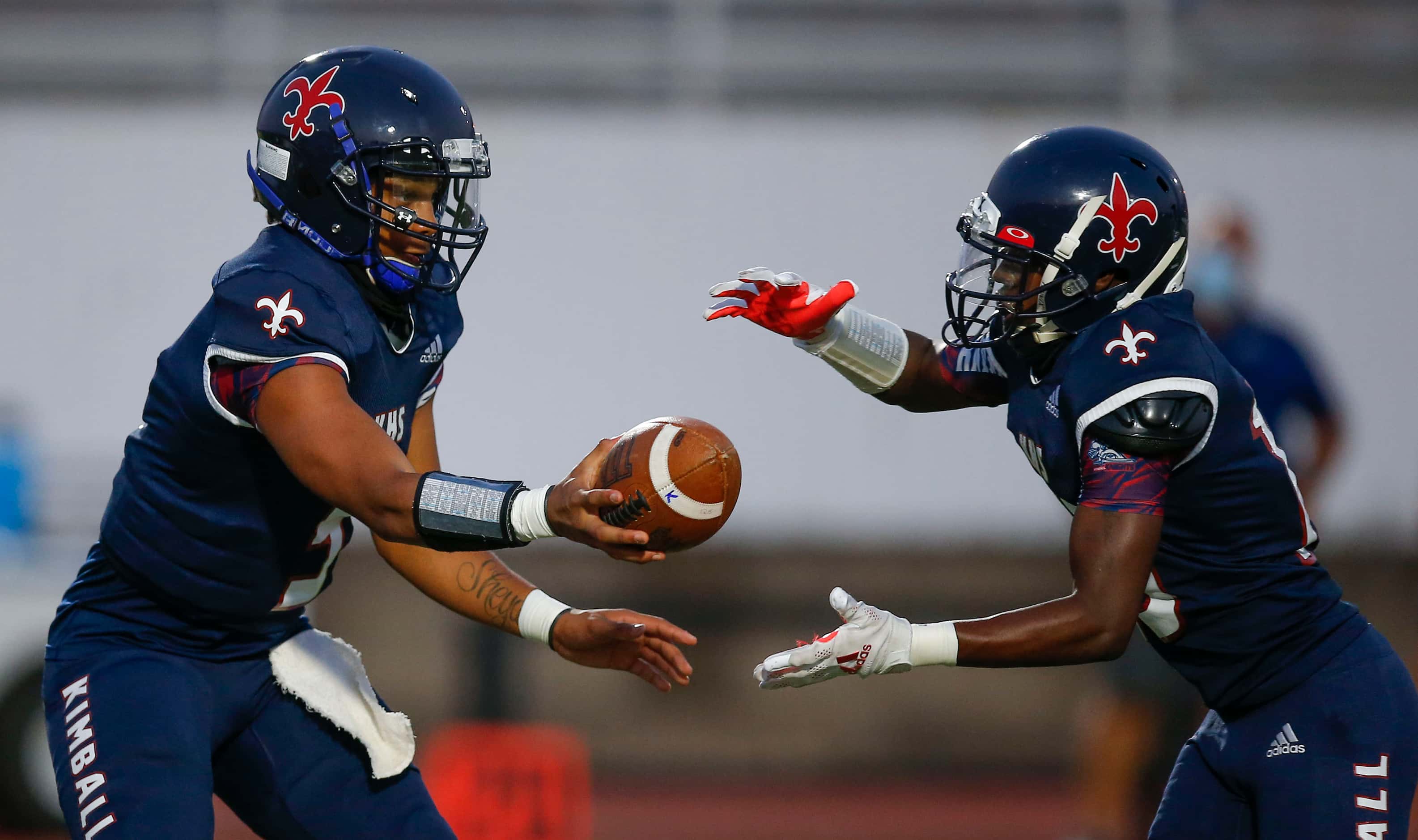 Kimball sophomore quarterback Jacarion Sauls, left, hands the ball off to junior running...