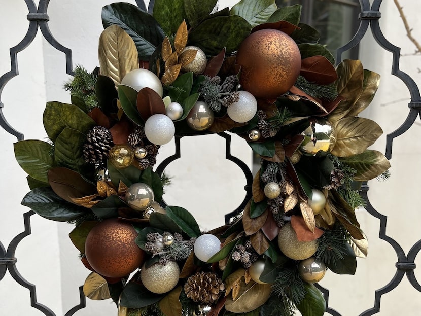 Faux wreath hanging on wire fencing has holiday baubles, metallic colors