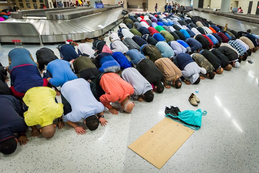 Muslim men set down their protest signs to pray at DFW International Airport where they...