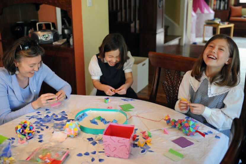 Deborah Adams, left, Katherine, 6, center, and Isabelle, 8, create origami ornaments to...