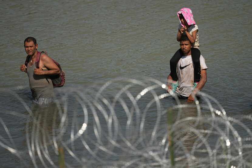 Migrants trying to enter the U.S. from Mexico stand in the Rio Grande behind concertina wire...