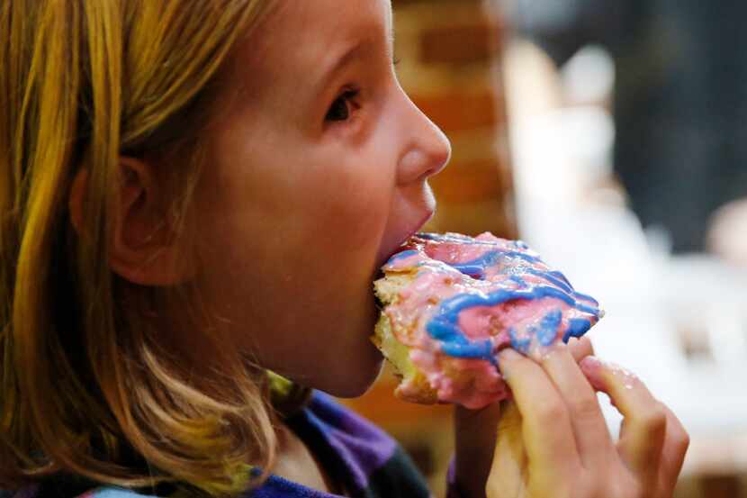 Cosette Ellis, 7 of Frisco takes a bite of a cotton candy donut during the grand opening at...