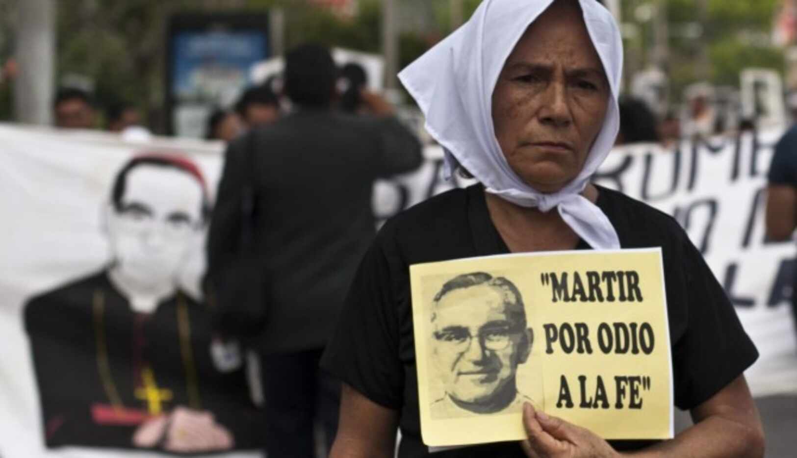 Una mujer carga una pancarta con el rostro del arzobispo Oscar Arnulfo Romero con la frase...
