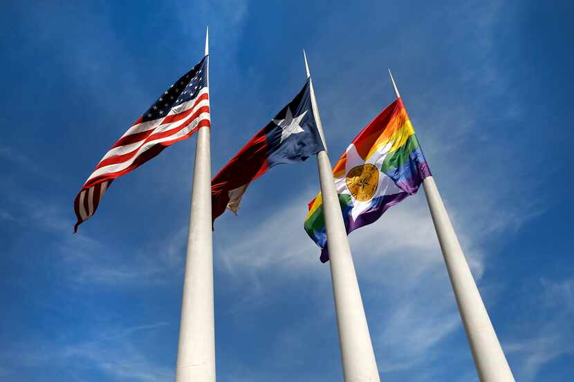 The City of Dallas' Pride flag (right) flies alongside the Texas and U.S. flags outside of...