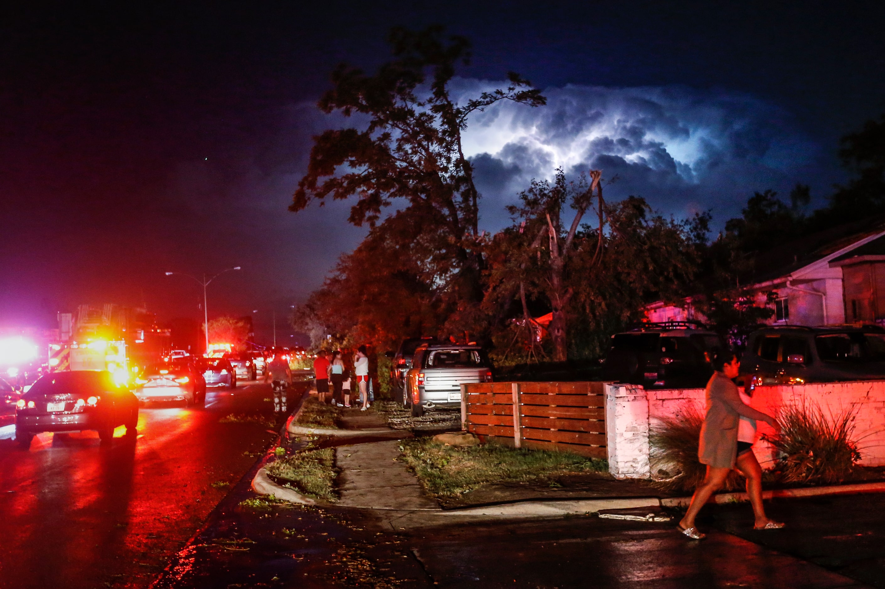 Lightning and emergency lights highlight damage as people gather in the parking lot of a...