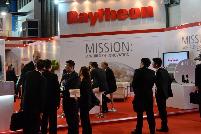 Trade visitors stand in front of a Raytheon booth during the Singapore Air Show on February...