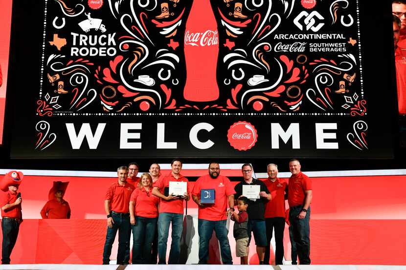 Winners of AC-CCSWB’s annual Truck Rodeo stand on a stage with a red background and a large...