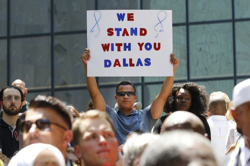 A man holds a sign reading "We Stand With You Dallas" during a vigil during a citywide...