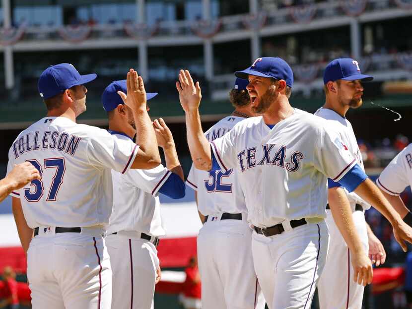 Texas Rangers starting pitcher Colby Lewis (48) slaps hands with teammates after being...