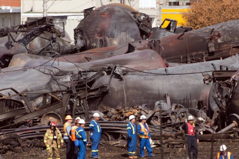 Workers stand before mangled tanker cars Tuesday, July 16, 2013, at the crash site of the...