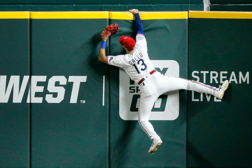 Texas Rangers right fielder Joey Gallo (13) hangs on the wall after attempting to catch...
