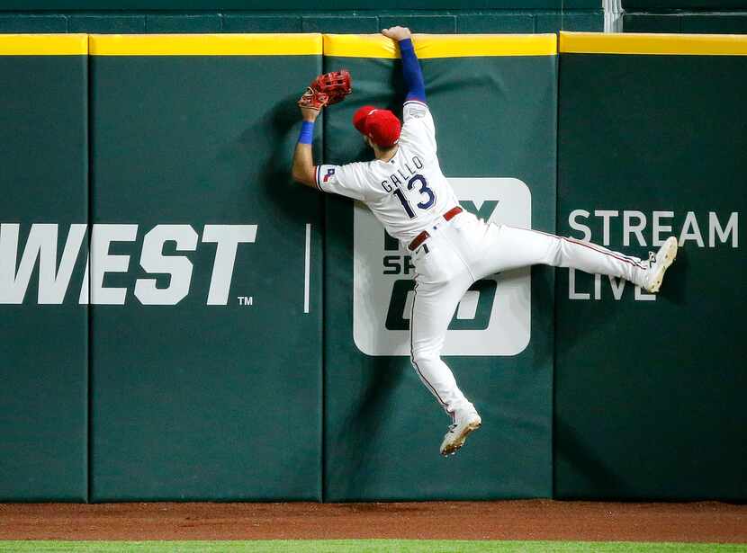 Texas Rangers right fielder Joey Gallo (13) hangs on the wall after attempting to catch...