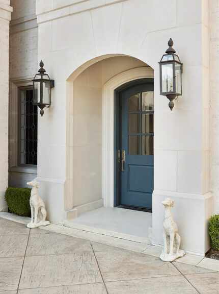 White stone doorway flanked by two dog statues and featuring a blue painted door