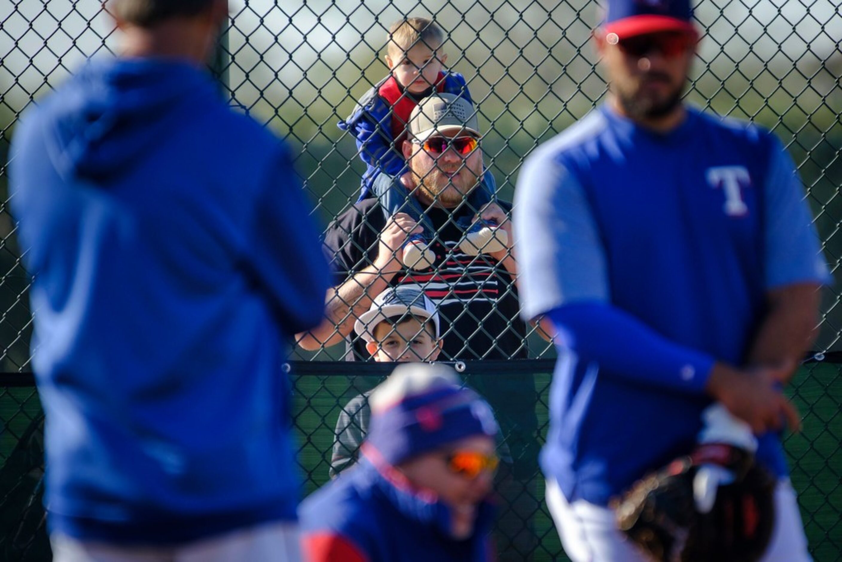 One-year-old Jaxon Shugart watches Texas Rangers catchers run a defensive drill from atop...