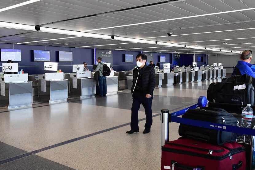 A man wears a facemask as he walks past empty United Airlines check-in counters at Los...
