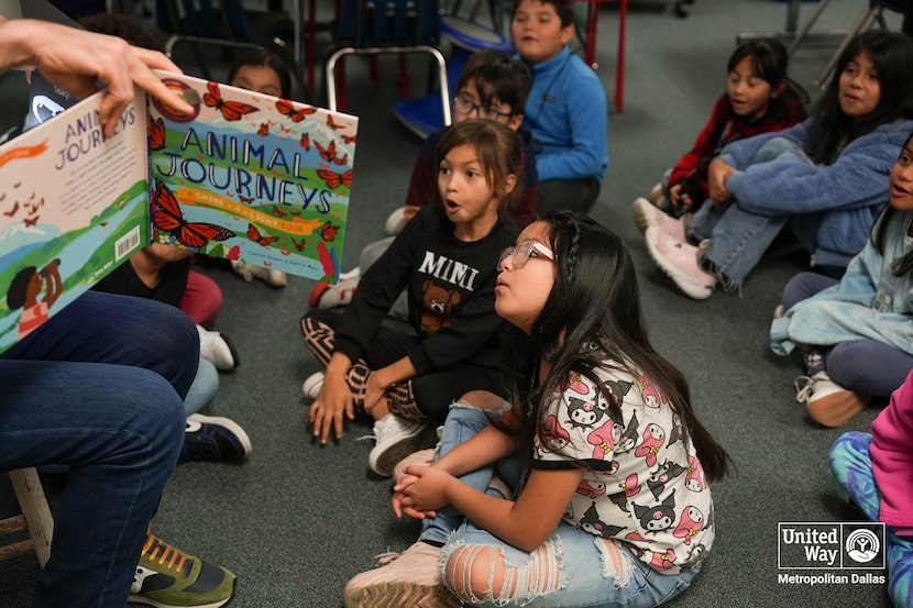 Elementary school children listen with interest as a volunteer reads to them from a book.