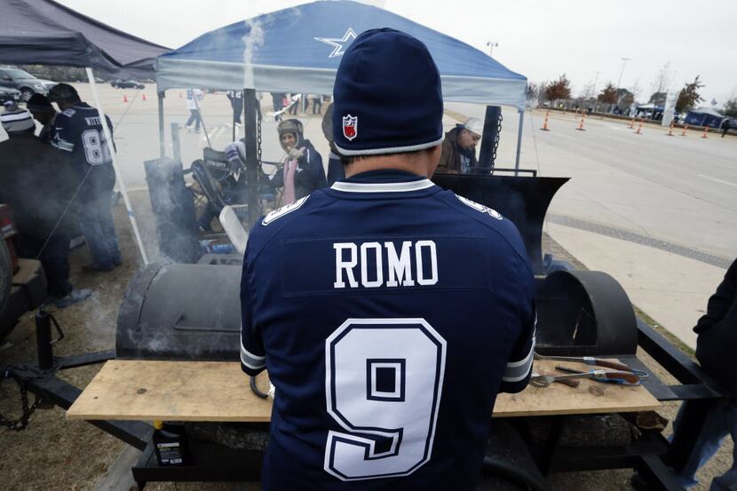 A Dallas fan dressed in a Tony Romo jersey warms himself near a grill on the AT&T stadium...
