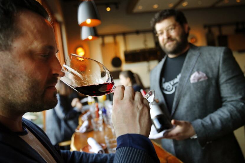 Rapscallion co-owner Bradley Anderson (left) noses a glass of red wine, just poured by his...