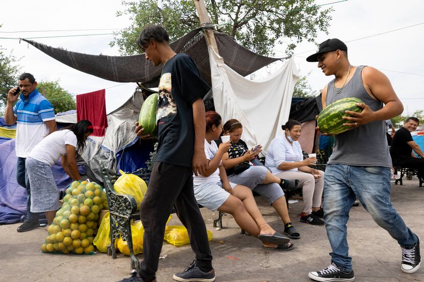 Migrants Jose Rivera (left) and Santo Manuel help a woman bringing fruit to sell at Plaza de...