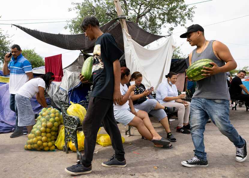 Migrants Jose Rivera, left, and Santo Manuel help a woman by carrying fruit at Plaza de la...