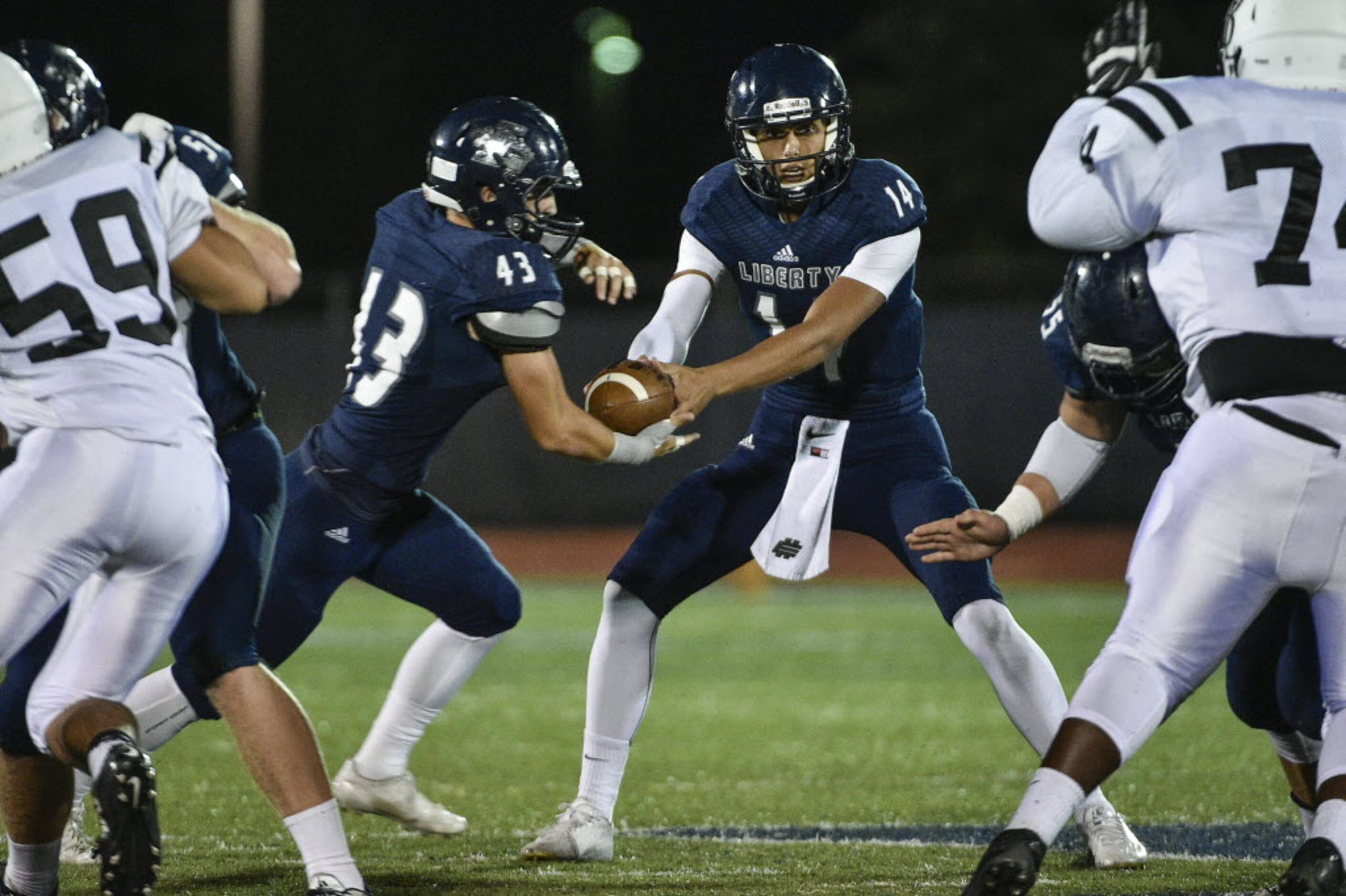 Liberty quarterback Nick Starkel (14) hands the ball to running back Cole Hawkins (43)...