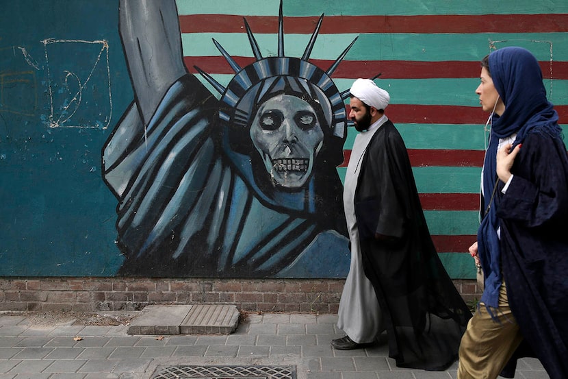 A cleric and a woman walk past an anti-U.S. mural painted on the wall of the former U.S....